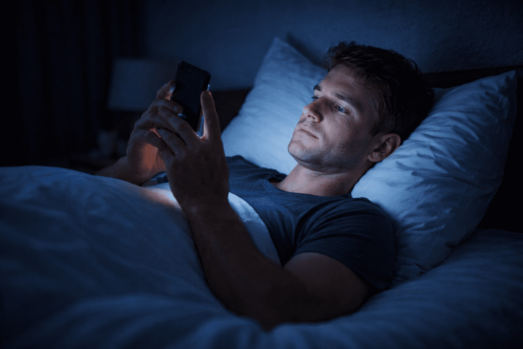 Adult scrolling phone in dark bedroom before sleep